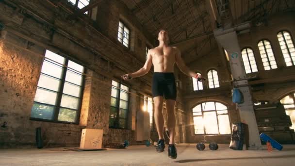 Sportovní cvičení muže bez košile s skákacím / skákacím lanem v opuštěné továrně Hardcore tělocvičně. Je pokrytý potem ze svého intenzivního tréninku křížové kondice. — Stock video
