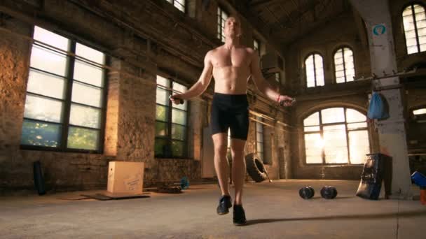 Sportovní cvičení muže bez košile s skákacím / skákacím lanem v opuštěné továrně Hardcore tělocvičně. Je pokrytý potem ze svého intenzivního tréninku křížové kondice. — Stock video