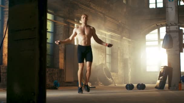 Sportovní cvičení muže bez košile s skákacím / skákacím lanem v opuštěné továrně Hardcore tělocvičně. Je pokrytý potem ze svého intenzivního tréninku křížové kondice.