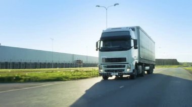 Açık görüş kamerası yarı kamyon kargo Trailer karayolu üzerinde sürüş ile izler. O hız aracılığıyla sanayi depo bölgesi ise güneş parlıyor ve diğer araçlar yolda.