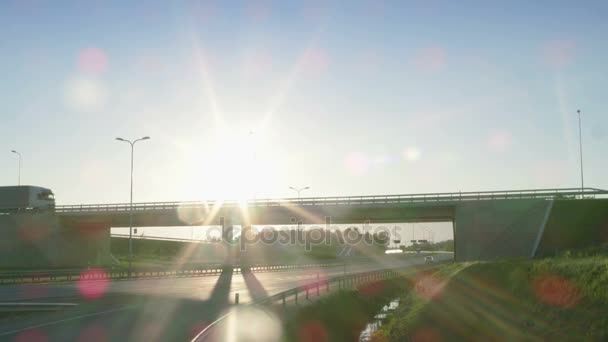Vista lateral de un semirremolque blanco con remolque de carga conduciendo a través de un puente. Hermoso paisaje con vehículo moviéndose en paso elevado mientras el sol está brillando y el cielo es azul . — Vídeos de Stock