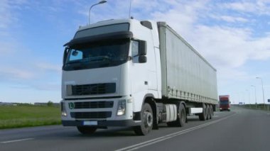 Hız beyaz yarı kamyon kargo römork ile karayolu üzerinde kullanıyor. Kamyon ilk ağır vasıtalar sütun, güneş Shining.