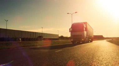 Kargo Treyler ile beyaz yarı kamyon sürücüleri boş yolda bağlı. Otoyol kenarlarında tarafından endüstriyel depolar. Günbatımı. 
