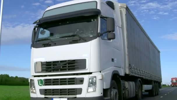 超速驾驶白色半卡车与货物拖车的正面视图字段与工业仓库在后台在高速公路上开车. — 图库视频影像