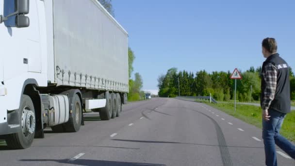 Водитель грузовика переходит дорогу и садится в свой припаркованный белый полугрузовик с прикрепленным грузовым трейлером. Солнечные лучи и шоссе пусты . Стоковое Видео