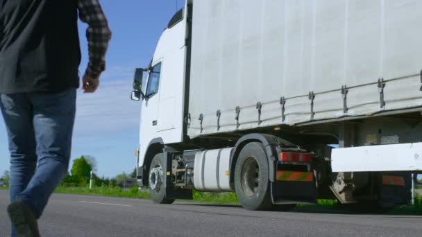 Motorista de caminhão atravessa a estrada na área rural e entra em seu caminhão semi-branco com reboque de carga anexado. Sol brilha e rodovia é vazio . — Vídeo de Stock