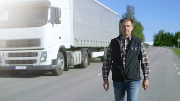 Professional kierowca wysiada z ciężarówki naczepy biały zaparkowane z dołączona przyczepa Cargo. Kierowca stoi na środku drogi i dumnie krzyże ramion. — Wideo stockowe