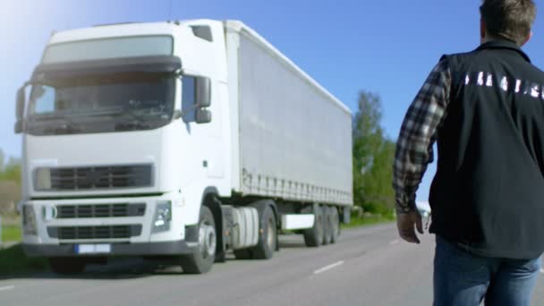 Camion driver attraversa la strada e ottiene nel suo parcheggiato bianco semi camion con rimorchio da carico allegato. Sole splende e autostrada è vuota . — Video Stock