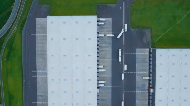 Zoom en plano aéreo de almacén industrial / edificio de almacenamiento / área de carga donde muchos camiones están cargando / descargando mercancías . — Vídeo de stock