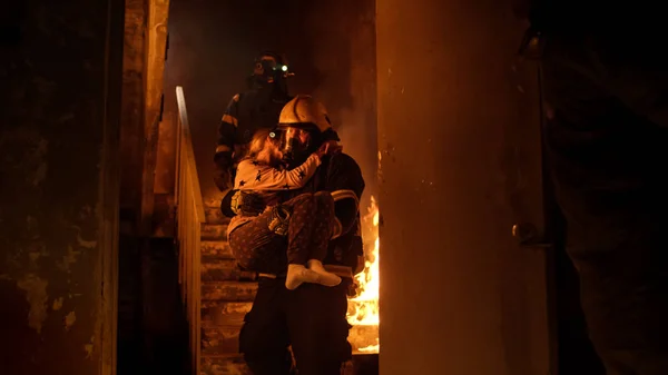 Valiente bombero desciende escaleras de un edificio en llamas con un salvado — Foto de Stock