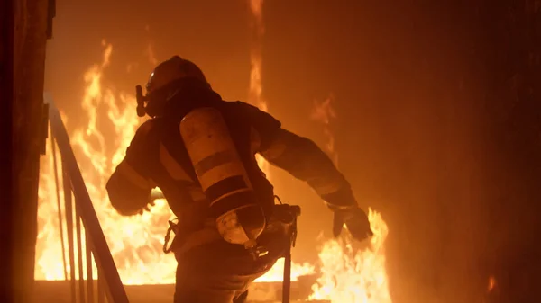 O corajoso bombeiro corre pelas escadas. Fogo furioso é visto em todos os lugares — Fotografia de Stock