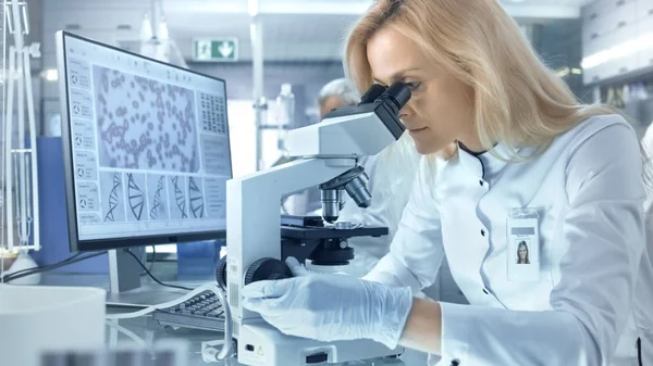 Женщина-исследователь рассматривает биологические образцы под микроскопом — стоковое фото