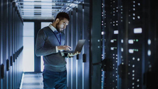 IT Technician Works on Laptop next to a Server Cabinet in Big Da
