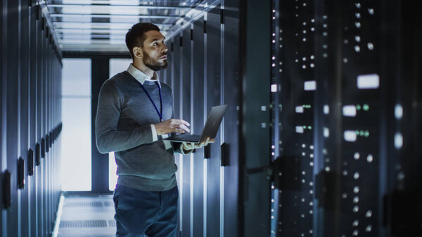IT Technician Works on Laptop next to a Server Cabinet in Big Da