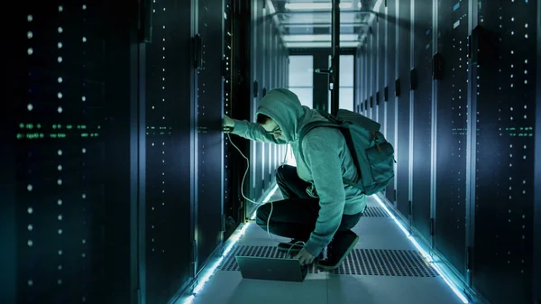 A Hooded Hacker With Laptop Connects to Rack Server and Steals I — Stock Photo, Image