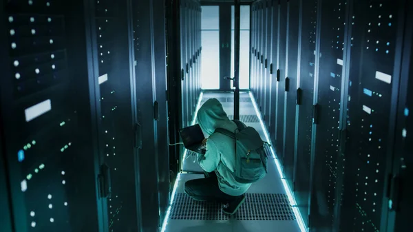 A Hooded Hacker With Laptop Connects to Rack Server and Steals I — Stock Photo, Image