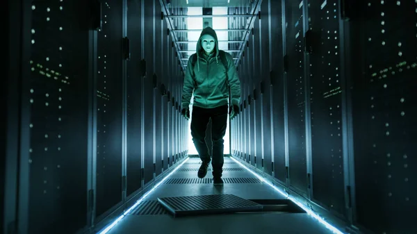 Hacker com capuz em uma máscara caminha através de centro de dados de trabalho com O — Fotografia de Stock