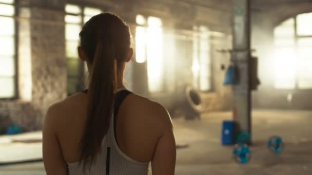 Acompanhamento Tiro de Atlético Mulher Bonita Entrando Ginásio em Movimento Lento. Ela é confiante e puxa seu rabo de cavalo, Edifício é Industrial e Hardcore, Vários Cross fitness / Musculação Equipamento deitado no chão . — Vídeo de Stock