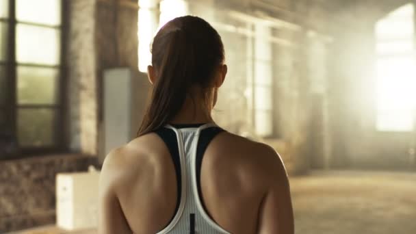 Folgebild einer athletisch schönen Frau, die in Zeitlupe das Fitnessstudio betritt. sie ist selbstbewusst, bauen ist industriell und hardcore, verschiedene Crossfitness- / Bodybuilding-Geräte liegen auf dem Boden. — Stockvideo