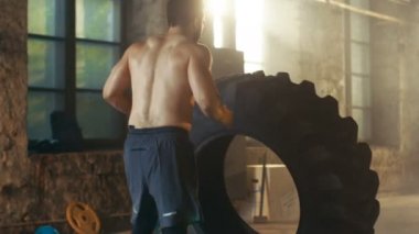 Güçlü kas adam arkadan görünüm asansörleri / lastik parçası onun vücut geliştirme / Fitness Eğitim çapraz olarak çevirir. O salona ter ve inşaat dışarı içinde terk edilmiş fabrikası Remodeled kaplıdır.