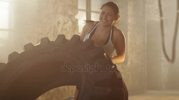 La donna atletica in forma solleva / capovolge lo pneumatico con grande sforzo come parte del suo allenamento di cross fitness / bodybuilding. Lavora nell'edificio abbandonato Remade come palestra . — Video Stock