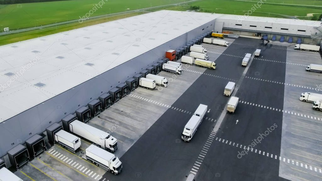 Aerial Shot of Industrial Warehouse/ Storage Building/ Loading Area where Many Trucks Are Loading/ Unloading Merchandise.