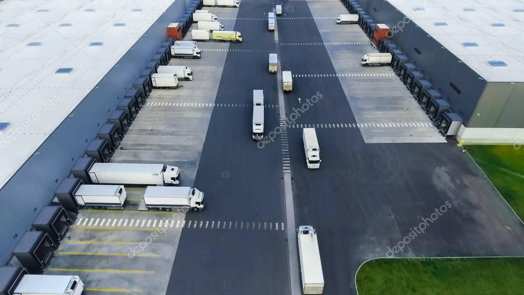 Aerial Shot of Industrial Warehouse/ Storage Building/ Loading Area where Many Trucks Are Loading/ Unloading Merchandise.