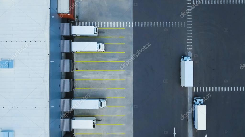 Aerial Shot of Truck with Attached Semi Trailer Leaving Industrial Warehouse/ Storage Building/ Loading Area where Many Trucks Are Load/ Unload Merchandise.