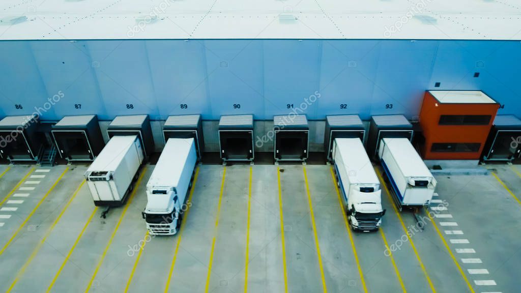 Aerial Side Shot of Industrial Warehouse Loading Dock where Many Truck with Semi Trailers Load/ Unload Merchandise.