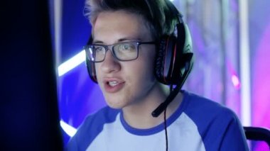 Genç çocuk oyun oynar, rekabetçi Video oyunundan bir esports turnuva / Internet Cafe. Gözlük ve kulaklık takıyor ve mikrofona konuşur.