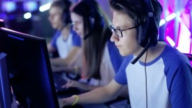 Profesyonel çocuk oyun oynar esports turnuva tarihinde Video oyununda / Internet Cafe. Gözlük ve kulaklık takıyor ve mikrofona konuşur. Diğer kızlar ve erkek oyuncu artalanda çalışır durumda.