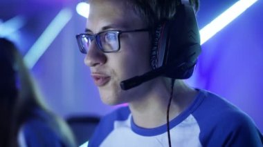 Profesyonel çocuk oyun oynar esports turnuva tarihinde Video oyununda / Internet Cafe. Gözlük ve kulaklık takıyor ve mikrofona konuşur. Diğer kızlar ve erkek oyuncu artalanda çalışır durumda.