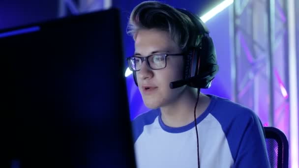 Young Teenage Boy Gamer Plays Video Game on a eSports Tournament/ Internet Cafe. He Wears Glasses and Headphones and Speaks into Microphone. — Stock Video