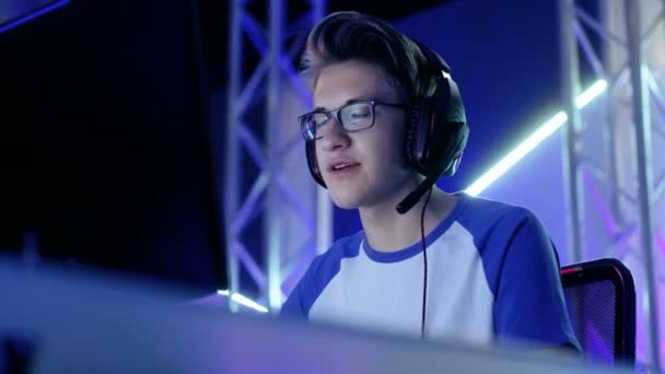 Nastoletni chłopiec Gamer odgrywa w konkurencyjnych gier wideo na esports turnieju / Internet Cafe. Nosi okulary i słuchawki i mówi do mikrofonu. — Wideo stockowe