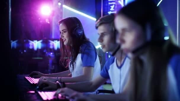Team professioneller E-Sport-Spieler, die in wettbewerbsfähigen Videospielen an einem Cyber-Games-Turnier teilnehmen. Mädchen und Jungen haben Kopfhörer auf, Arena ist mit Neonlicht beleuchtet. — Stockvideo