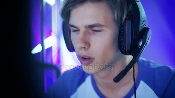 Close-up Shot of Professional Boy Gamer Plays in Video Game on a eSports Tournament / in Internet Cafe. Ele usa fones de ouvido e dá comandos no microfone . — Vídeo de Stock