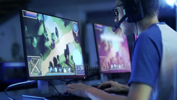 Jugador profesional juega en MMORPG / Estrategia de videojuegos en su ordenador. Participa en torneos de ciberjuegos en línea, juega en casa o en Internet Café. Lleva gafas y auriculares para juegos . — Vídeo de stock