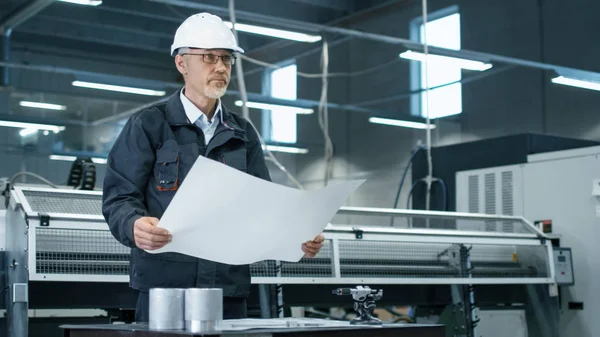 Ingénieur senior en casque est debout dans une usine et à la recherche — Photo