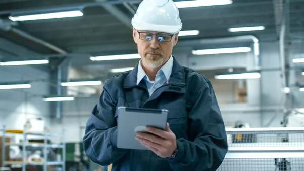Senior engineer in hardhat is using a tablet computer in a facto — Stock Photo, Image