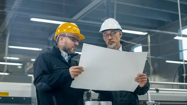 在戴安全帽的两名工程师讨论站在一幅蓝图 — 图库照片