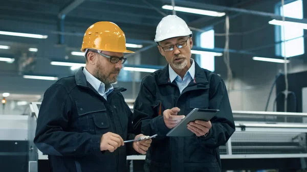 Hardhats で 2 人のエンジニアがタブレット コンピューター上の情報を話し合う — ストック写真