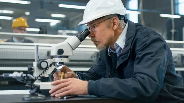 Leitender Ingenieur inspiziert ein Detail unter dem Mikroskop in einer Fabrik — Stockfoto