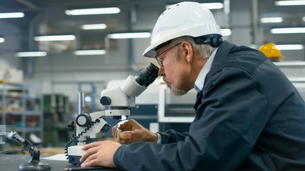 Ingeniero superior está inspeccionando un detalle bajo el microscopio en un fac — Foto de Stock