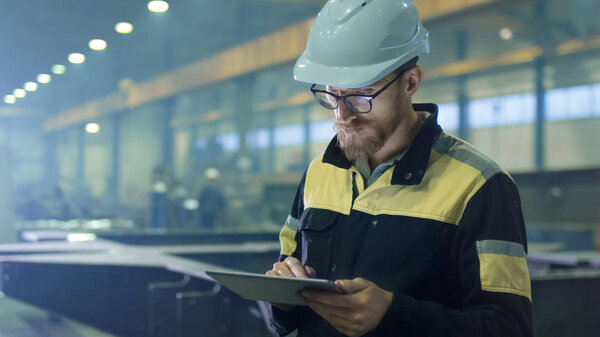 Engineer in hardhat is using a tablet computer in a heavy indust