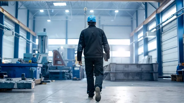 Trabalhador da fábrica em um chapéu duro está andando através de facil industrial — Fotografia de Stock