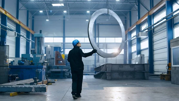 Trabajador de fábrica en un sombrero duro está moviendo un detalle de metal con un rem — Foto de Stock