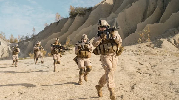 Escouade de soldats armés entièrement équipés qui courent dans le désert. S — Photo