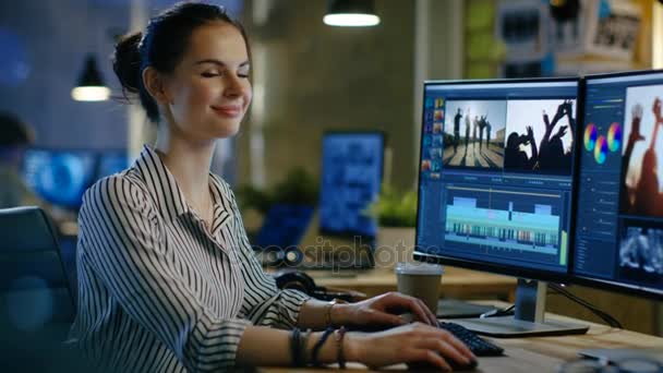 Female Video Editor Works with Footage and Sound on Her Personal Computer, She Turns and Warmly Smiles into the Camera Ее кабинет - современный и креативный лофт-студия . — стоковое видео