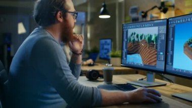 Yaratıcı erkek oyun geliştiricisi yeni seviye tasarımı için grafik ile inşaat, iki görüntüleme kişisel bilgisayarda çalışma onun tahta masada oturuyor. Diğer insanlar iş bu yaratıcı Studio.