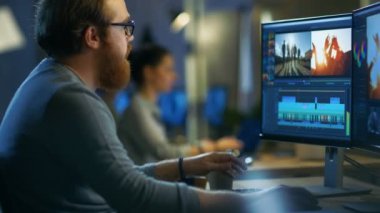 Erkek Video Editor görüntüleri ve ses ile iki göstermek onun kişisel bilgisayarda çalışır. O diğer yaratıcı insanlarla serin Office çatı katında çalışıyor.